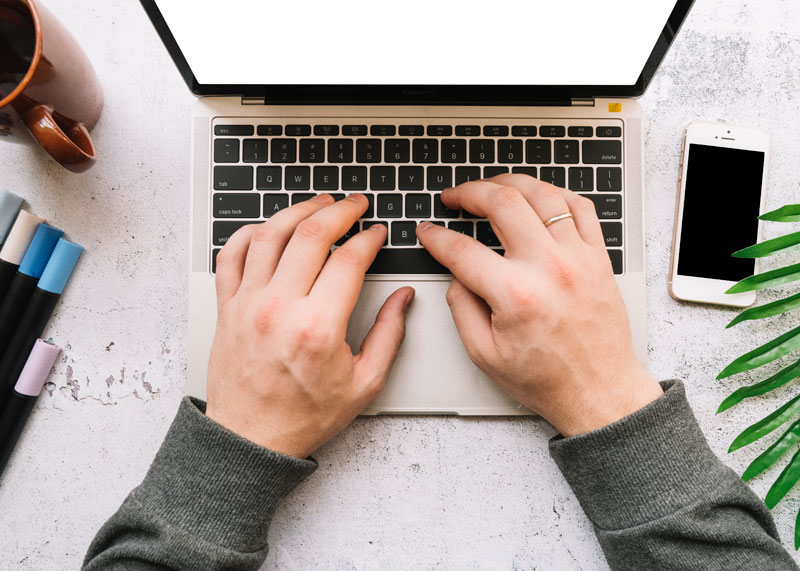 Aufgeklappter Laptop auf einen Tisch mit Handy sowie Stiften und einer Tasse