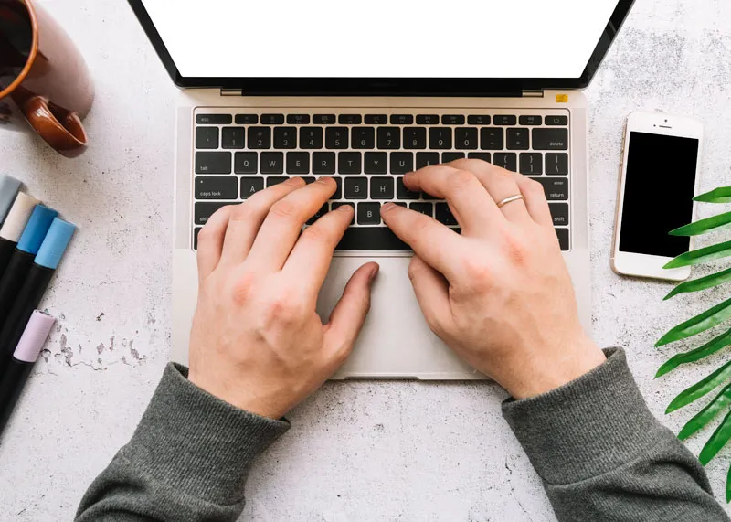 Aufgeklappter Laptop auf einen Tisch mit Handy sowie Stiften und einer Tasse